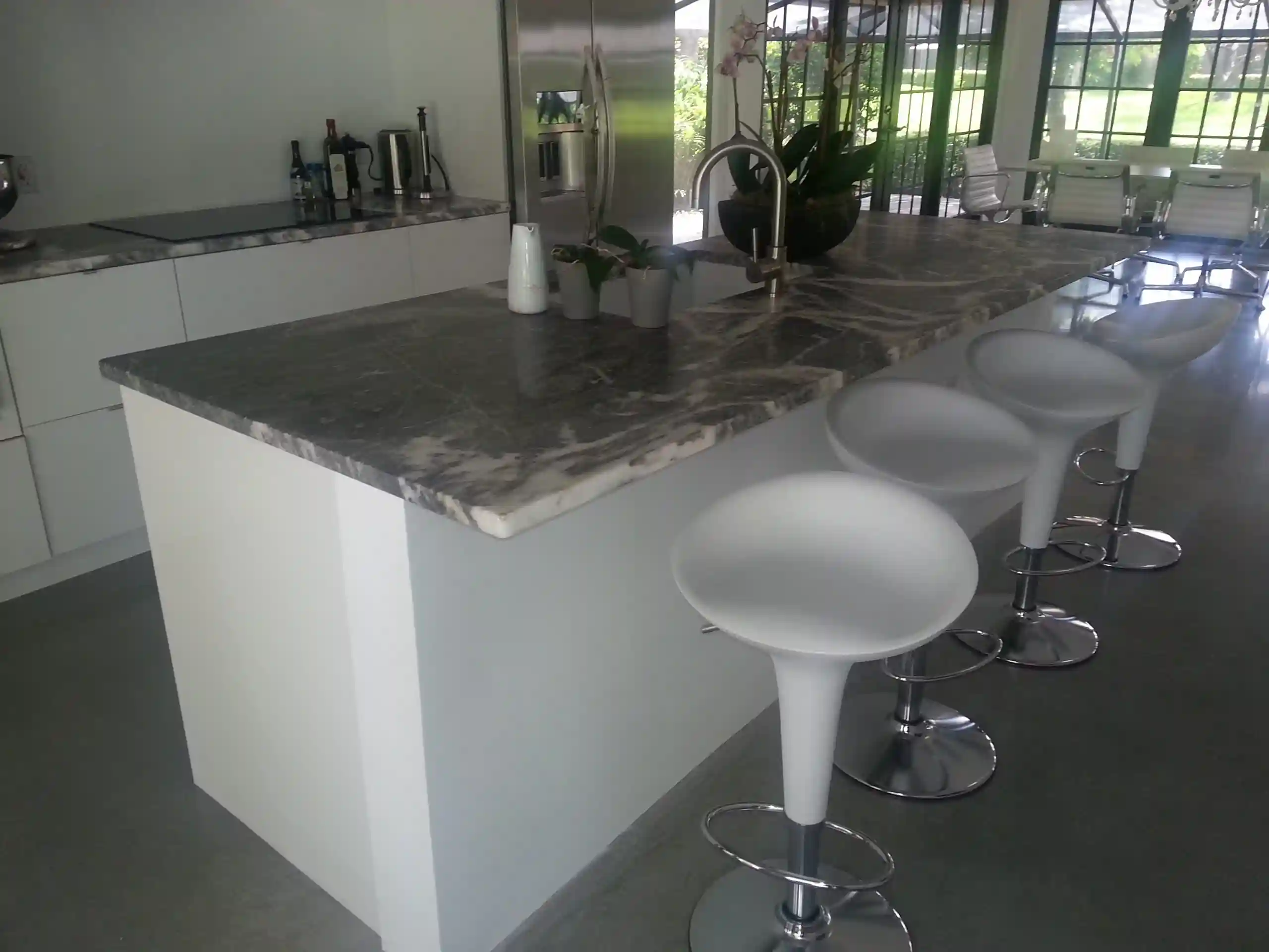 Modern kitchen renovation with a marble waterfall island, sleek white cabinetry, stainless steel appliances, and contemporary bar stools in an open-concept layout.
