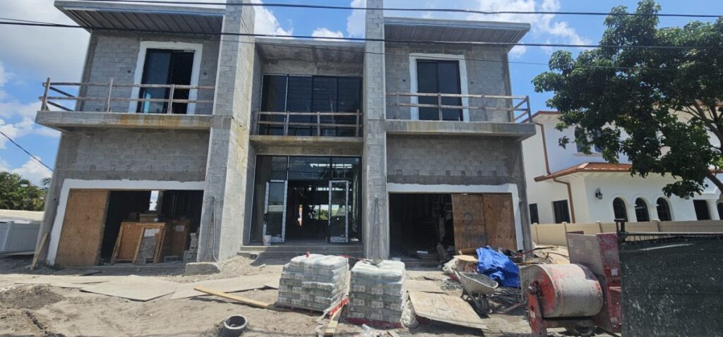 A two-story concrete building under construction with open garage bays and construction materials in the foreground.