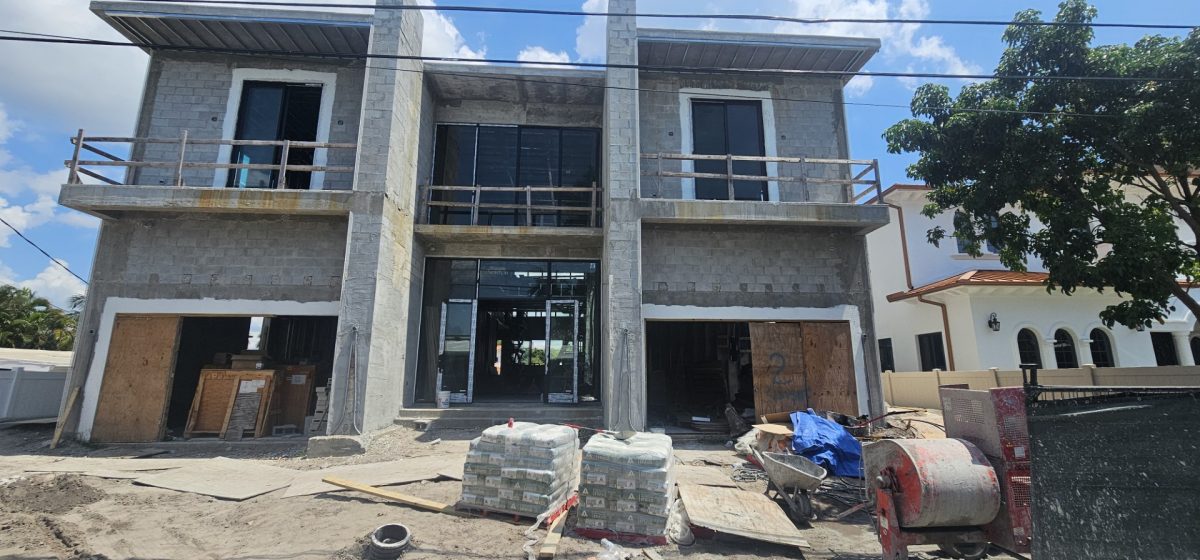 A two-story concrete building under construction with open garage bays and construction materials in the foreground.