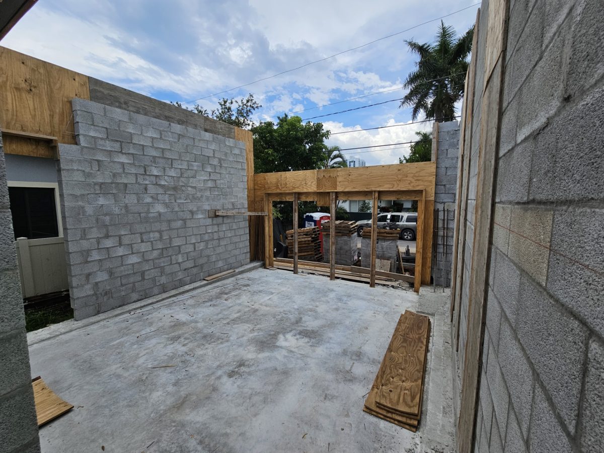 An unfinished room with concrete block walls, a poured concrete slab floor, and plywood framing for a large exterior opening.